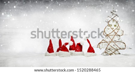 six little red santa claus hats in the snowed ground with a decoration christmas tree, with snowflakes in the grey sky background, a beautiful picture for the cold winter december christmas time