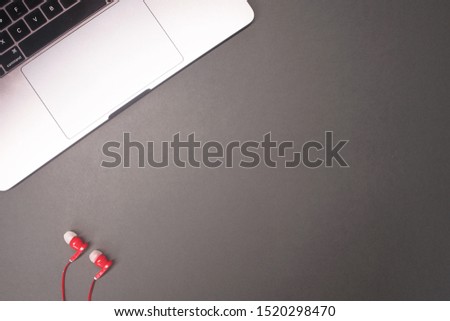 Top view of work place desk, laptop with  red earphones on empty dark grey background, minimalism