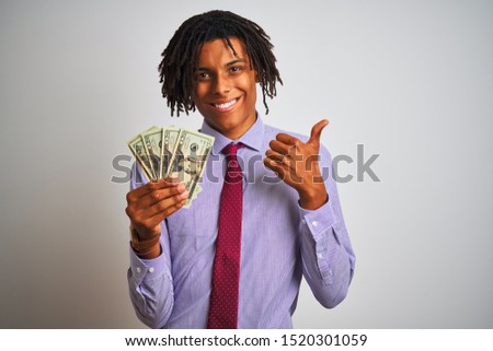 Afro american businessman with dreadlocks holding dollars over isolated white background happy with big smile doing ok sign, thumb up with fingers, excellent sign