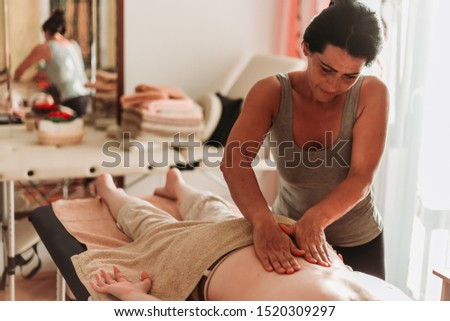 Close-up photo of masseuse massaging her client back. Red spa light. Relaxation concept