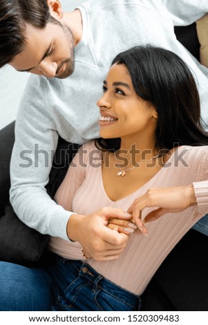 high angle view of african american woman and handsome man smiling and holding hands in apartment 