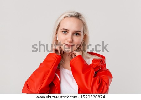 Pretty blond girl wearing red raincoat and white t-shirt dancing listening to music with wireless earbuds. Concept of enjoying life.