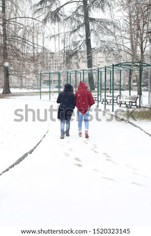 two women walking alone in a city park in a snowy day