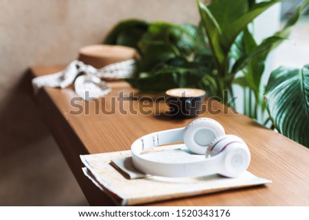 Image of cup of coffee, headphones, passport, paper map lying on wooden table in cafe indoors