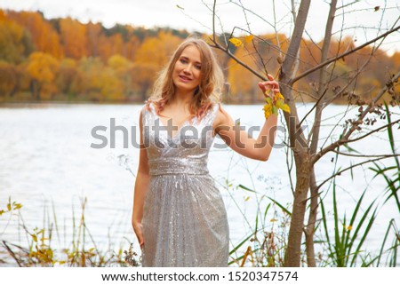 beautiful plus size girl in silver long dress posing near the pond in the autumn city Park alone