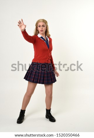 
full length portrait of blonde girl wearing red cardigan with tie and plaid skirt, school uniform, standing,  walking  pose facing the camera, on a white studio background