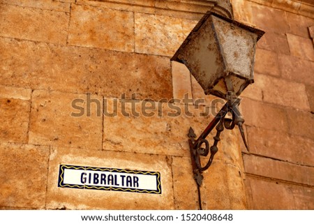 Gibraltar: inscription on an old stone wall. Rusty antique floor lamp hanging next to it.