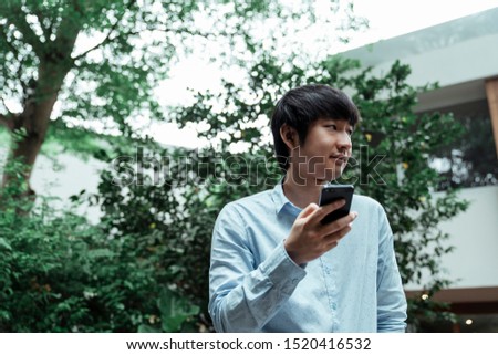 A man in blur shirt holding his phone while standing in a garden of cafe.