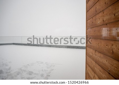 Wooden wall on terrace covered by snow at cable car station Birg on Schilltorn mountain with foggy background and copy space