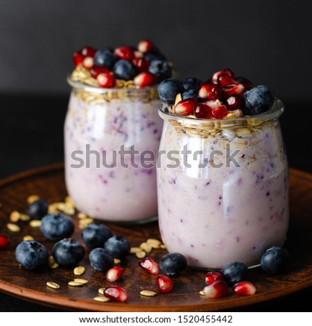 Close up shot of yogurt with blueberries, pomegranate seeds and oats on dark background. Front view, square image