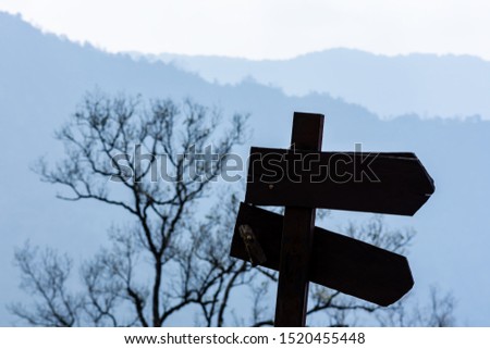 The signpost is on the mountain, with trees and mountains behind.
