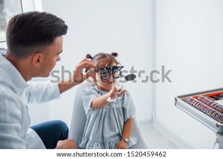 Testing vision. Young ophthalmologist is with little female visitor in the clinic.