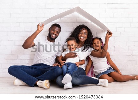 Family Housing Concept. Young African American Parents With Two Children Sitting Under Cartboard Roof Dreaming Of New Home, Copy Space Royalty-Free Stock Photo #1520473064