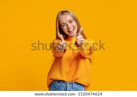 I like it. Portrait of joyful teenage girl showing thumbs up and smiling at camera, orange background with copy space Royalty-Free Stock Photo #1520474624