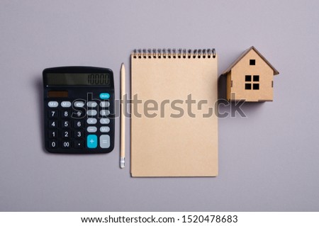 House model with brown notebook, pencil, calculator on gray background, top view