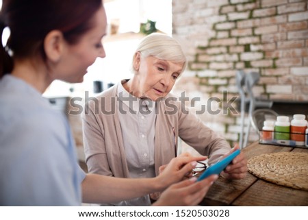 Woman feeling involved. Aged woman feeling involved in using tablet with her helpful caregiver