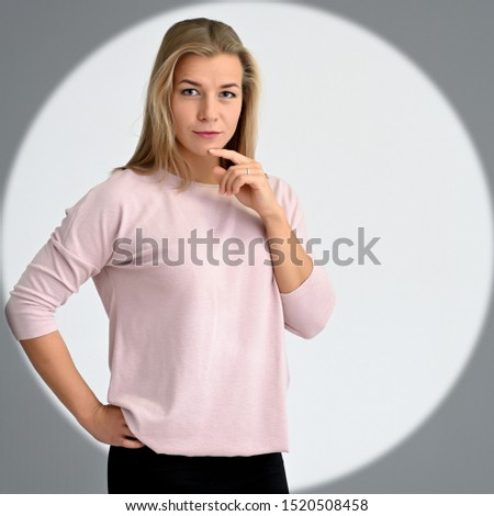 Concept portrait of a cute smiling beautiful student blonde woman girl in a pink sweater in a circle of light. A wide smile, excellent teeth.