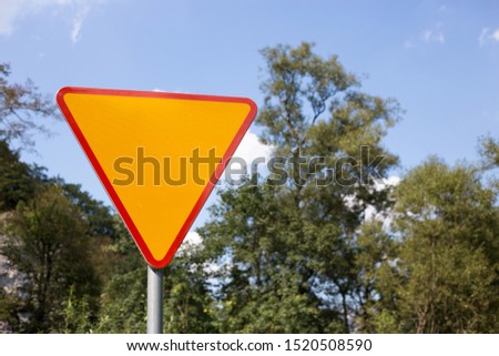 Blank yellow triangle road sign on the road, nature background