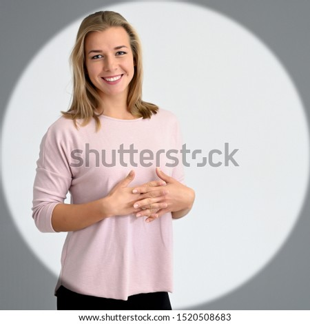 Concept portrait of a cute smiling beautiful student blonde woman girl in a pink sweater in a circle of light. A wide smile, excellent teeth.