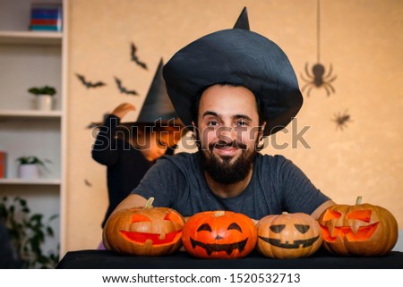Happy family: father and daughter celebrate Halloween. Cheerful children in carnival costumes indoors at the table with pumpkins. Cheerful child and parents play with pumpkins and black witch hats