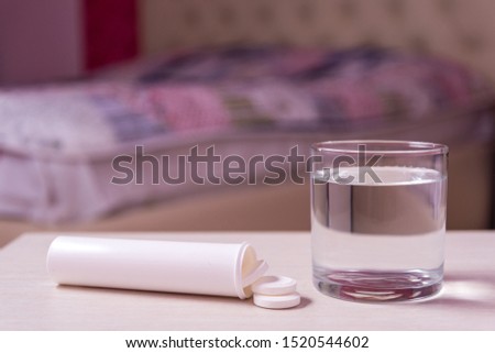 A glass of water and a tube of soluble effervescent tablets on the blurred background of the bed in the bedroom.Treatment and prevention of viral diseases. Help with depression and insomnia.copy space