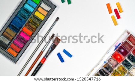 Flat lay art materials on white paper, tassels, pencils, watercolors, pastel art materials