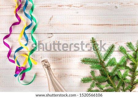 Winter Christmas composition with champagne bottle, pink, yellow, green, blue curly satin ribbons and spruce branch on white wooden background. Flat lay, top view, copy space