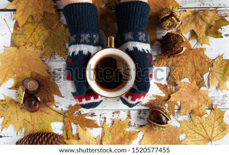 Autumn mood. Yellow, orange maple leaves on a wooden background and a cup of coffee in the hands. A lot of dry leaves and chestnuts, a hot drink, warm mittens, comfort. Natural materials