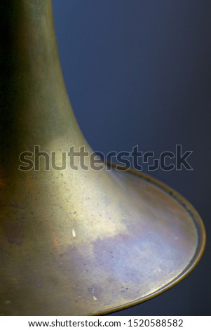 Bass trombone bell close up on dark background.  Vintage instrument with no lacquer, raw brass with wear and tear, scratches and blemishes.  Portrait orientation.