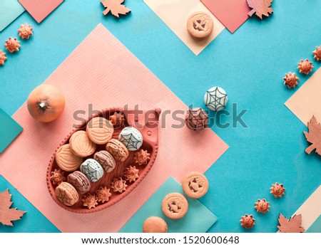 Halloween background with pumpkin cookies, macaroons and maple leaves on split geometric paper background in pastel colors