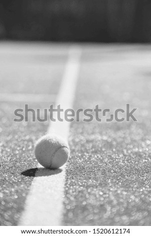 Black and White photo of a close up of a Tennis ball on red court during sunny day