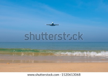 The plane flies over the Mai Khao Beach in thailand. Below is soft sand and a blue sea with nice waves.