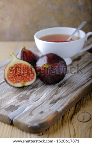 Fresh ripe figs and a white cup of tea on a wooden table. 