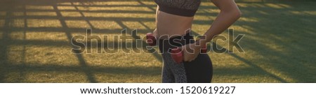 A young slim athletic girl in sportswear with snakeskin prints performs a set of exercises. Performs exercises with dumbbells. Fitness and healthy lifestyle. Panoramic image banner, toned.