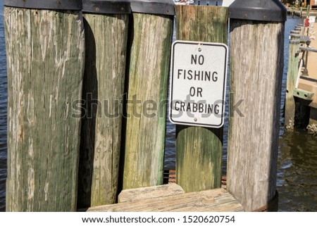 Grunge no fishing or crabbing sign on weathered wooden pier on sunny waterfront.