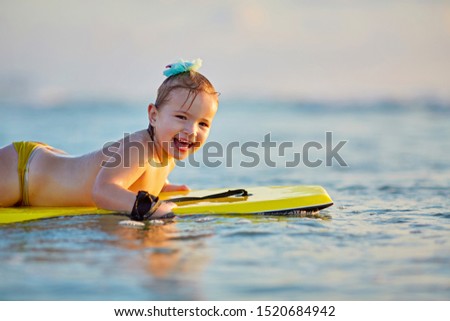 foamy waves of the beautiful autumn sea splashing alongside a charming little girl on a yellow surfboard in a sunny sunset