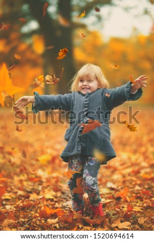 Happy little girl throwing yellow autumn leaves in the air in the park; autumn background 