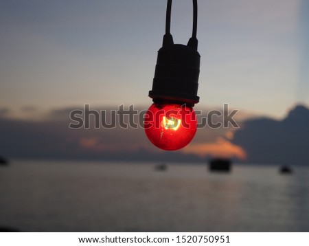 Glowing red light bulb hanging on wire on evening sky background. 