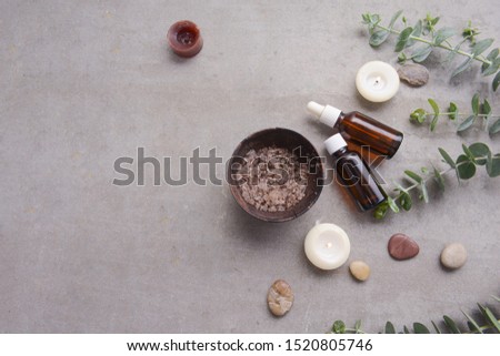 Eucalyptus leaves and two candle and , salt in bowl ,spoon bottles of essential oil ,on gray background
