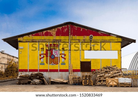 Close-up of the national flag of Spain
 painted on the metal wall of a large warehouse the closed territory on a summer day. The concept of storage of goods, entry to a closed area, tourism