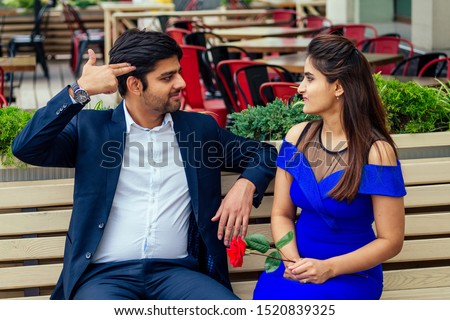 long haired brunette indian woman in blue dress with her handsome boyfriend having dating getting bored .man giving rose to his girlfriend bad relationship in summer downtown street.