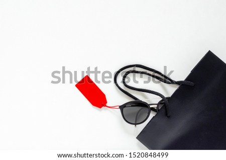 Flat lay of black sunglasses with red price tags and shopping bag on white background for Black Friday sale concept.
