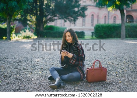 girl using her cell phone while walking through the park during autumn