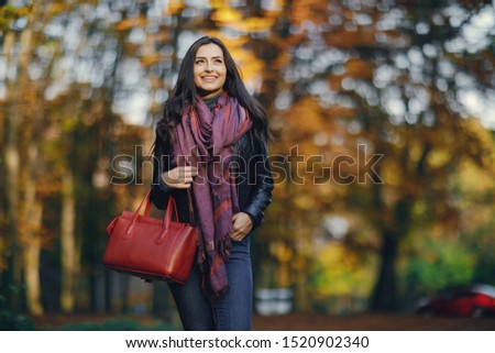 brunette girl using her phone as she is relaxing at the park during autumn