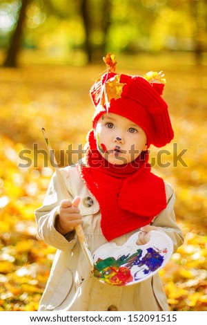 Child painting on easel in Autumn Park. Little Girl in Red Hat, Creative kids drawing development concept.