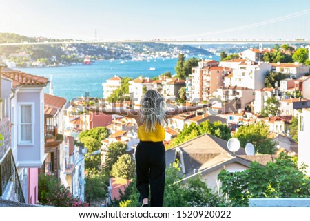 Blonde tourist woman is standing on the hill with open arms and looks towards the Istanbul Bosphorus in Kuzguncuk. Kuzguncuk is a neighborhood in the Uskudar district in Istanbul, Turkey. Royalty-Free Stock Photo #1520920022
