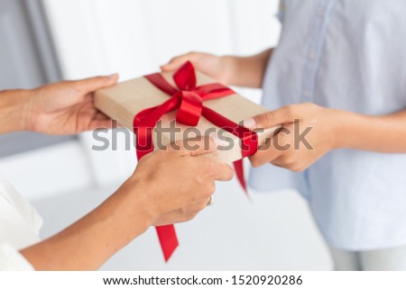 Closeup of thin gift box in hands of mother and daughter. Selective focus
