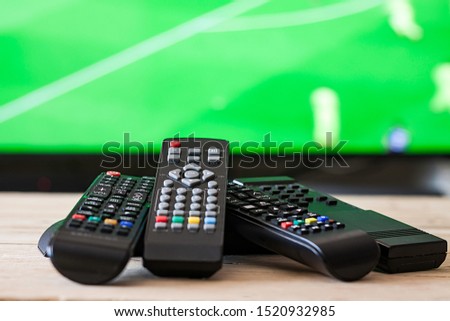 REMOTE CONTROLS ON TABLE AND TELEVISION TO THE FUND. LOOKING THE FOOTBALL MATCH Royalty-Free Stock Photo #1520932985