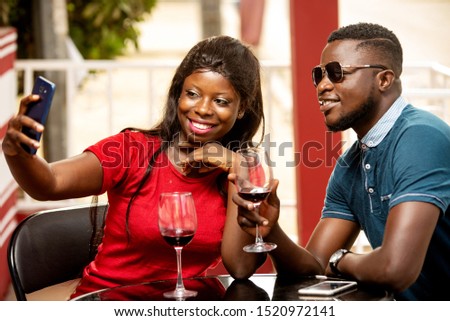 young couple sitting outside a refreshment booth photographing themselves with a mobile phone while smiling.