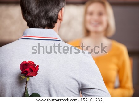 Surprise for her. Rear view of man holding rose behind his back while standing in front of his smiling wife
